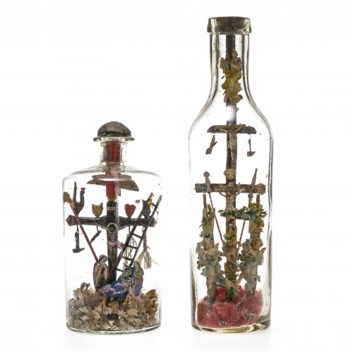 Flascheneingerichte, zwei Teile. Süddeutsch, Ende 19. Jh. Farbloses Glas, darin Holzarbeit, bemalt und mit Druckbildern dekoriert. Mit Arma Christi. Leicht besch. H. 20-31 cm.