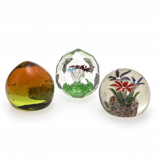 Drei Paperweights. 20. Jh. Bayerischer Wald. Farbloses Glas, eines vielkantig geschliffen. Mit farbigen, floralen Einschmelzungen. Dritter Briefbeschwerer in gelb-grün und honigbraun, mit schimmernden Plättchen im Inneren. Leichte Kratzspuren. H. 9-7,5 cm.